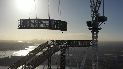 Crane lifting huge steel girder to join with a massive steel structure on roof top of skyscraper.